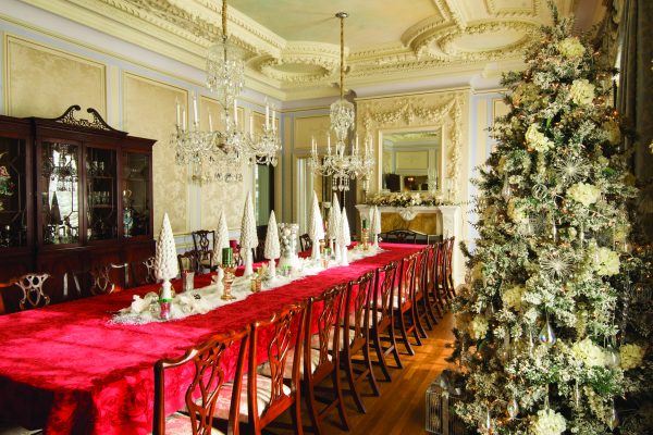 GLANWORTH GARDENS: The dining room décor corresponds with the large tree in the Great Hall. Placed upon the red poinsettia tablecloth are tapered white Christmas trees mixed with silver and white ornaments as well as white poinsettias. 
