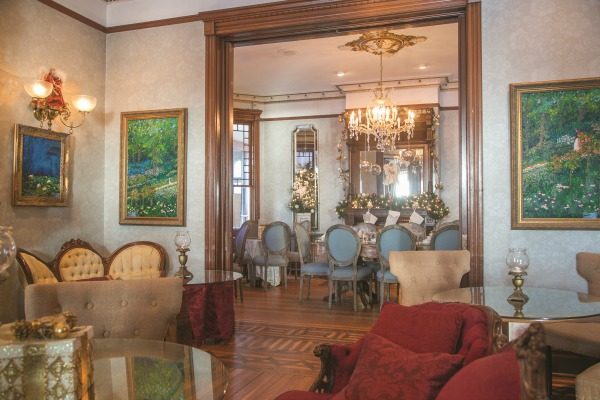 Furniture in the music room includes pieces that represent the period when the house was completed in 1885, including Eastlake styles featuring rich, red velvet upholstery. Paintings in the impressionist style by local artist Weston Courier flank the large entryway to the dining room.