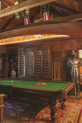 Displaying an impressive collection of curiosities, including a suit of armor, old slot machine and cowboy holster, the billiard room’s dark paneling and vaulted ceiling are a dramatic backdrop to a vintage canoe turned chandelier hung over the pool table. 