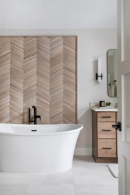 A custom-designed wall installation made of reclaimed wooden chevron tiles provides a stunning focal point behind the tub in the primary bath.