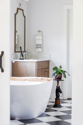 In the primary bathroom, black-and-white checkerboard floors bring a touch of vintage glam, contrasting the curving lines of the modern soaking tub. To keep the effect bright and modern, Loobeek selected a white oak vanity. To add a touch of personality to the space, Loobeek added an equestrian- themed plant stand she found during a thrifting expedition. She says that adding greenery to any space helps to freshen up
a space. The house features Kohler fixtures throughout.