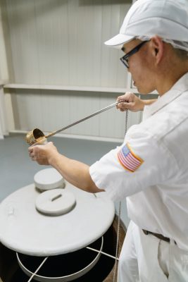 Inside the plant, soy sauce
is fermented in large drums. Frequently during the process, the product is tested for quality. Finished soy sauce is bottled
in the iconic teardrop bottle. Inspectors ensure the bottled soy sauce meets Kikkoman’s high standards of presentation.  Photo courtesy Kikkoman Foods Inc.